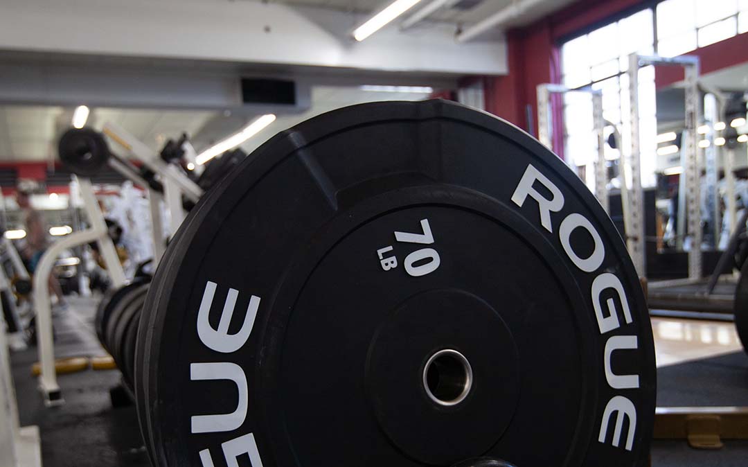 Fitness plateau in NJ: Close-up of a 70LB Rogue Plate with a glimpse of the gym in the background, photo taken during the day.